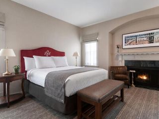 A cozy hotel room with a red headboard, white linens, and a fireplace, creating a warm and inviting atmosphere.